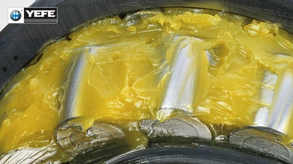 Close-up of yellow waterproof grease fully encapsulating roller bearings, showcasing its thick, cohesive structure that resists water washout, prevents corrosion, and maintains lubrication under continuous exposure to rain, humidity or salt spray — engineered with calcium sulfonate thickeners for maximum durability in harsh marine environments.