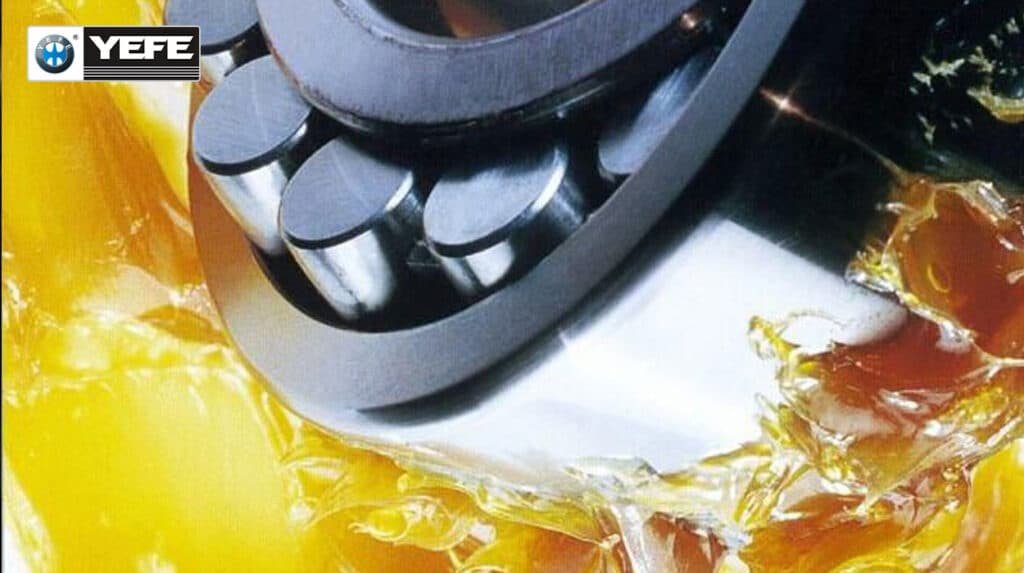 Roller bearing with golden YEFE grease showing excessive oil bleeding and dripping from rollers and raceway, demonstrating a common grease failure mode where structural breakdown from over-greasing, contamination or incompatibility causes loss of retention and lubrication film failure.