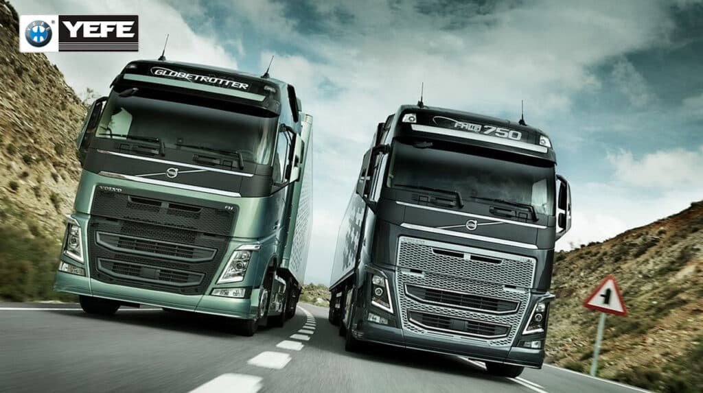 Two Volvo FH series heavy-duty trucks — a green Volvo FH Globetrotter on the left and a black Volvo FH16 750 on the right — cruising on a mountain highway under a dynamic sky; this image represents the demanding operating conditions of long-haul commercial transport, where engines face sustained high loads, elevated temperatures, and extended drain intervals, making the use of specialized diesel engine oil like YEFE Sports CF-4/E3 20W-50 critical for maintaining oil film strength, controlling soot, and protecting against wear in high-performance truck engines.