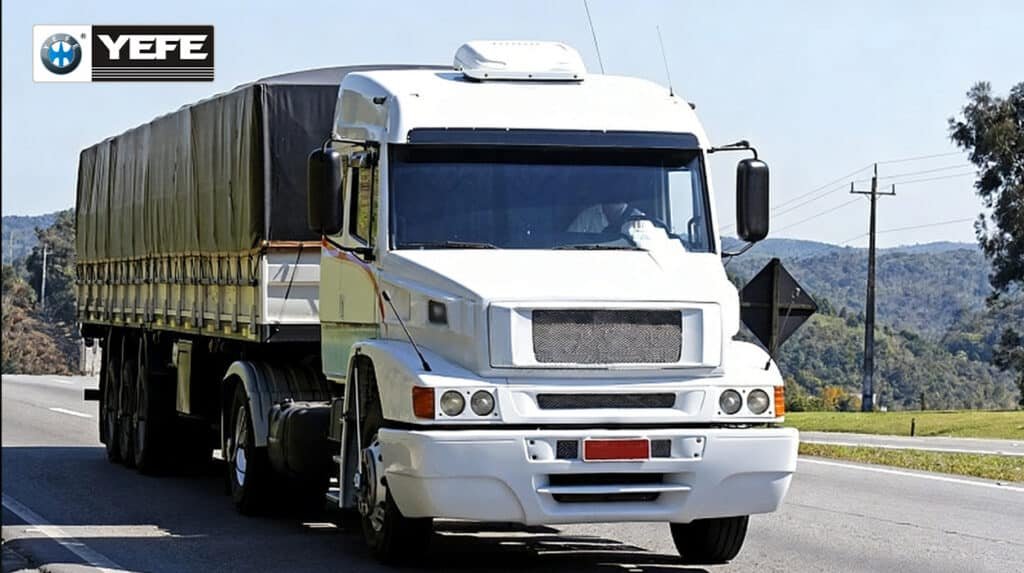 White heavy-duty semi-truck with canvas-covered cargo trailer driving on a rural highway, representing real-world fleet operations where YEFE engine oils deliver reliable protection against heat, soot, and wear under continuous load and varying terrain conditions.